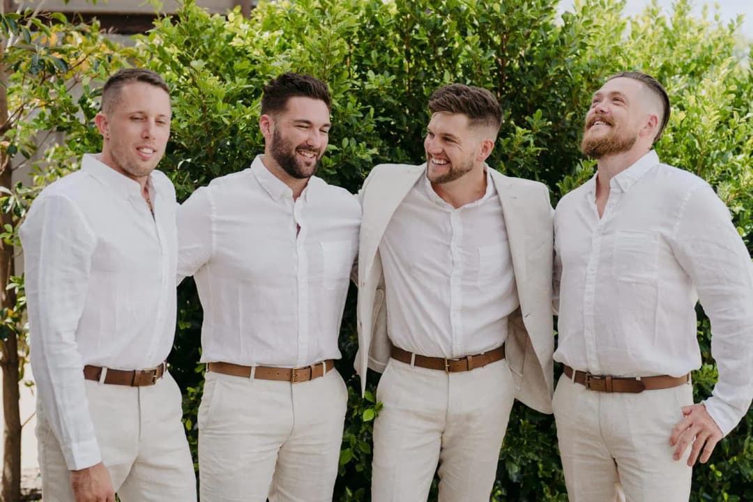 Four men smiling together with their arms around each other in a garden