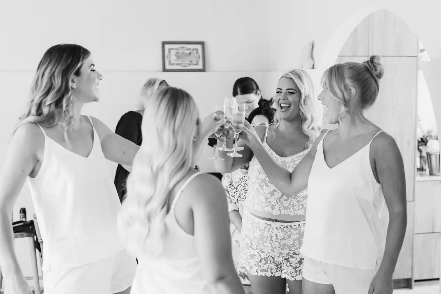 Black and white photograph of women raising glasses together while getting ready