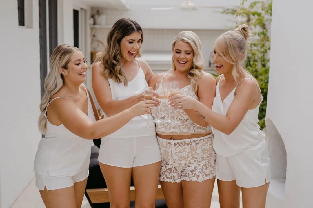 Four women raising glasses together in a sunny outdoor passage