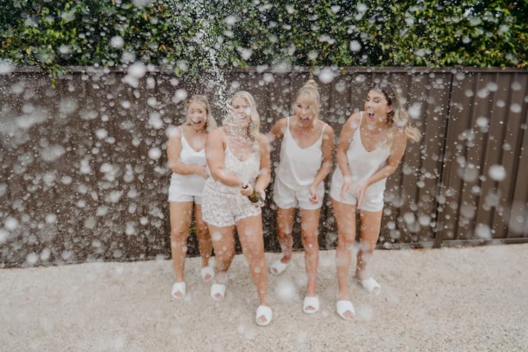 Women laughing through a spray of sparkling wine outdoors
