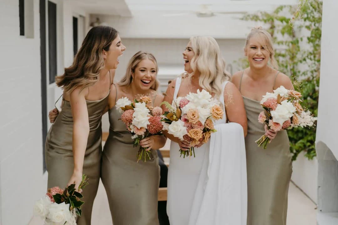 Bride and three bridesmaids laughing together with peach and white bouquets