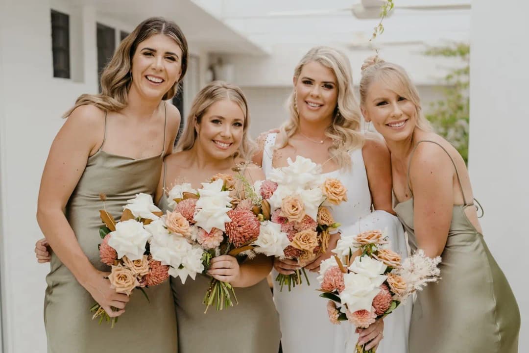 Bride and bridesmaids smiling together with bouquets in an outdoor passage