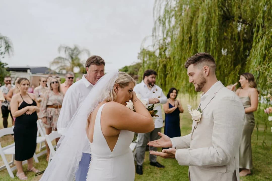 Bride wiping her eye as the groom reaches toward her at the ceremony