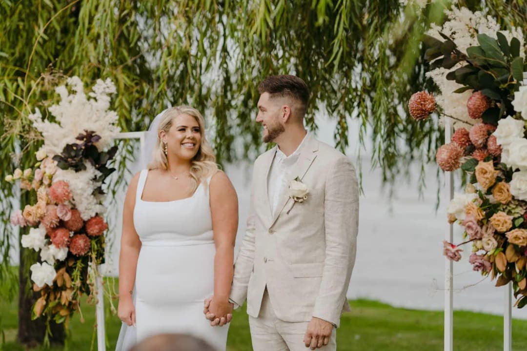 Bride and groom smiling at each other between tall floral stands