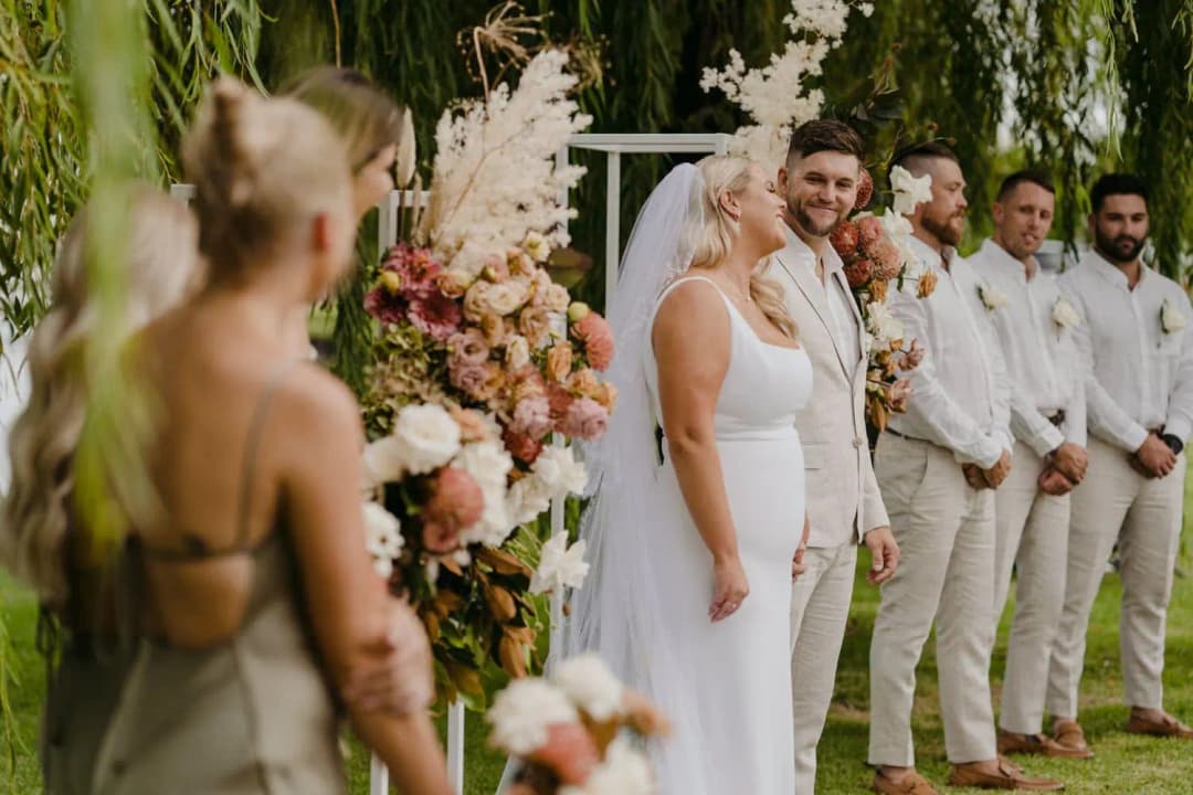 Bride and groom standing together as a bridesmaid speaks in the foreground