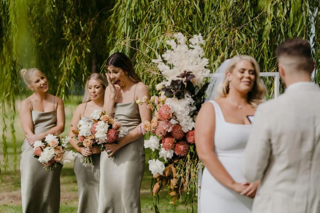 Bridesmaids smiling with their bouquets behind the bride and groom