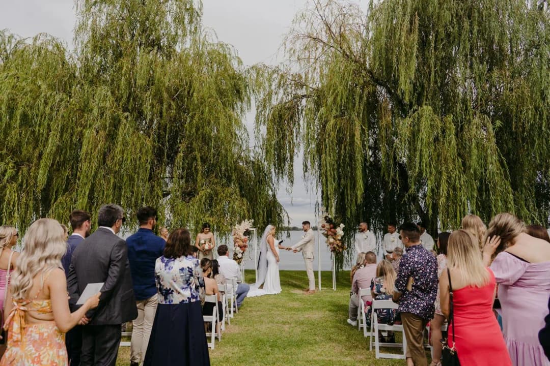 Guests standing beside white chairs at the lakeside ceremony