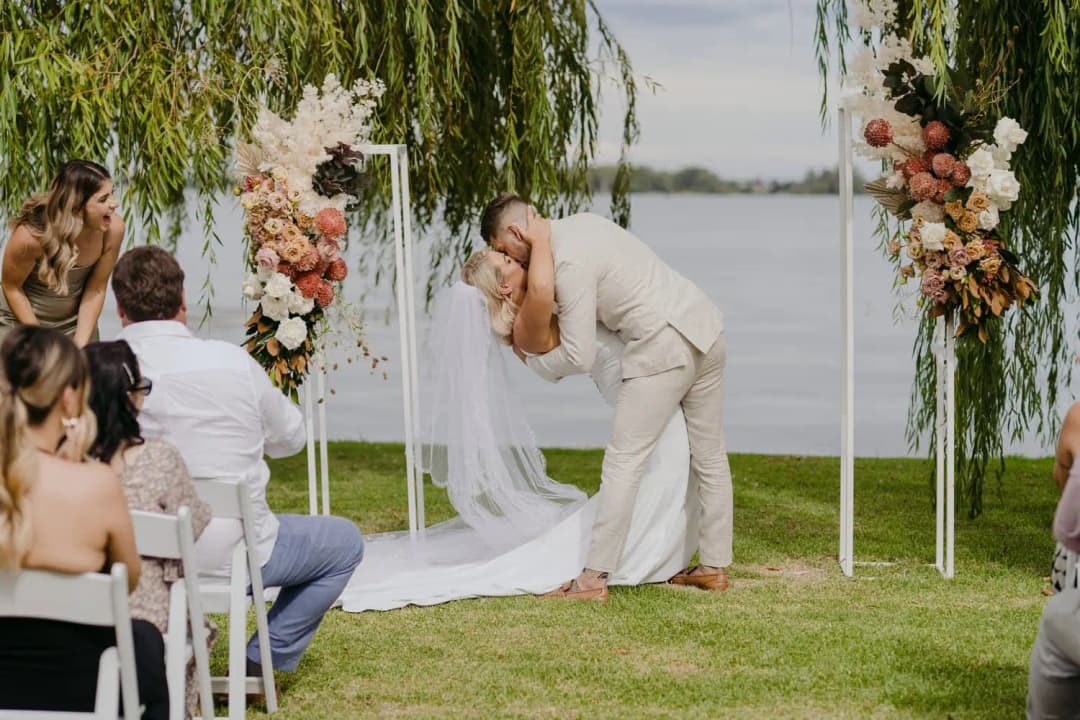 Groom dipping the bride into a kiss beneath willow branches