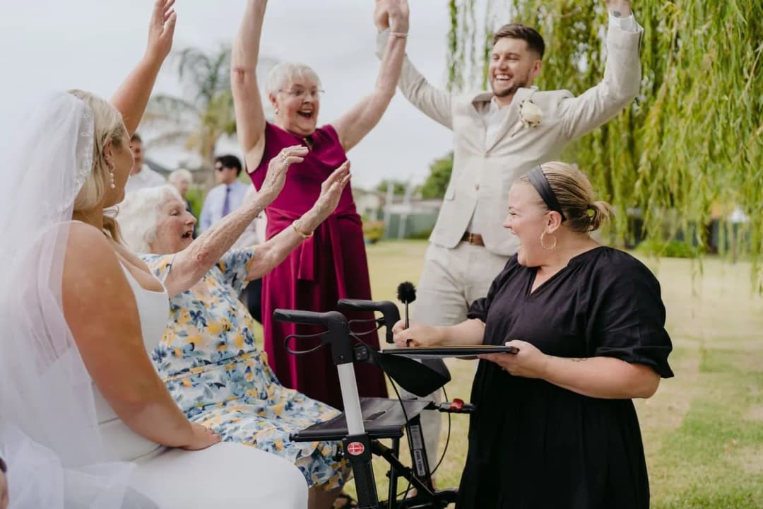 Bride and groom celebrating with guests and the celebrant beneath a willow tree