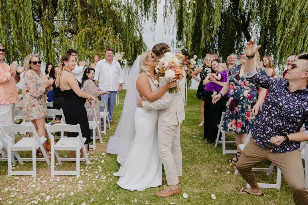 Bride and groom kissing in the aisle as guests cheer around them