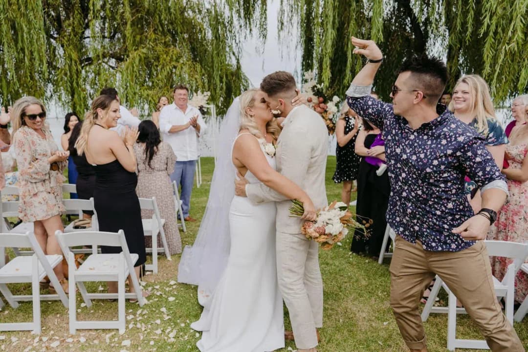 Bride and groom smiling together as a guest raises his arm in celebration