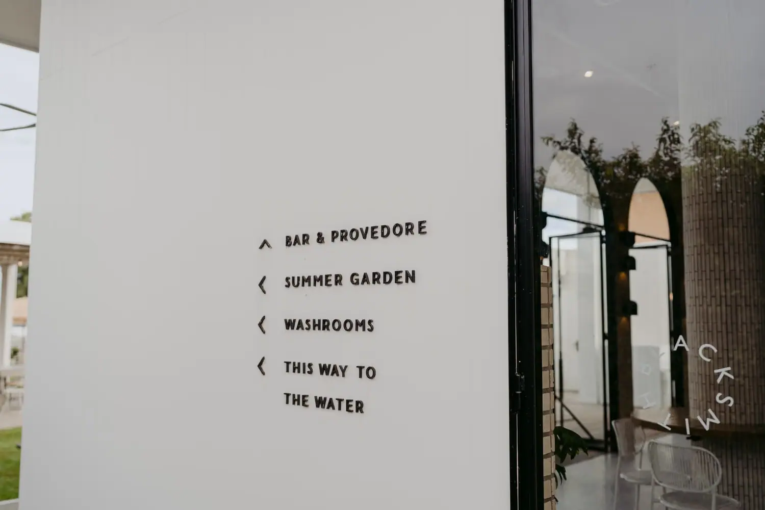 Directional signs for the bar, garden, washrooms and waterfront beside a glass door