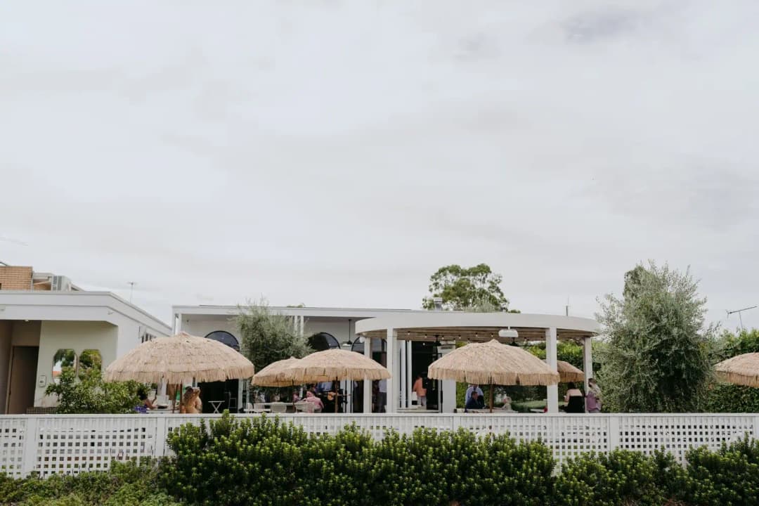 Outdoor reception venue with shaded seating behind a white fence