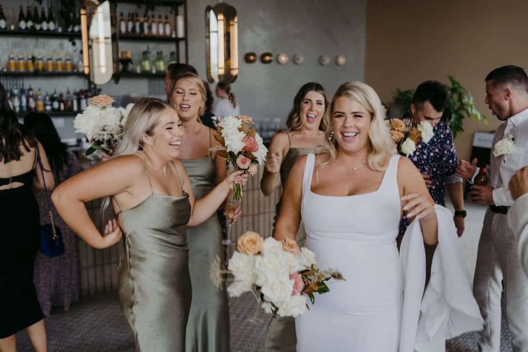 Bride and bridesmaids laughing with bouquets inside the reception bar