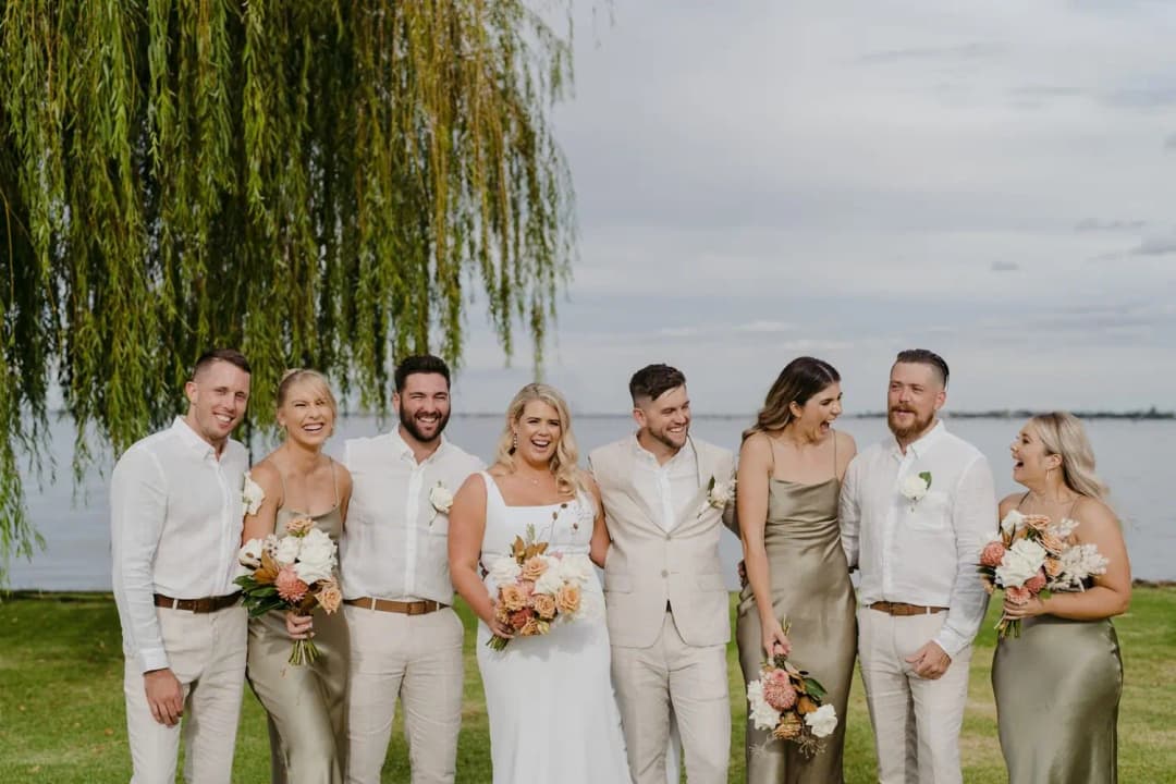 Wedding party posing together beneath a willow tree beside the lake