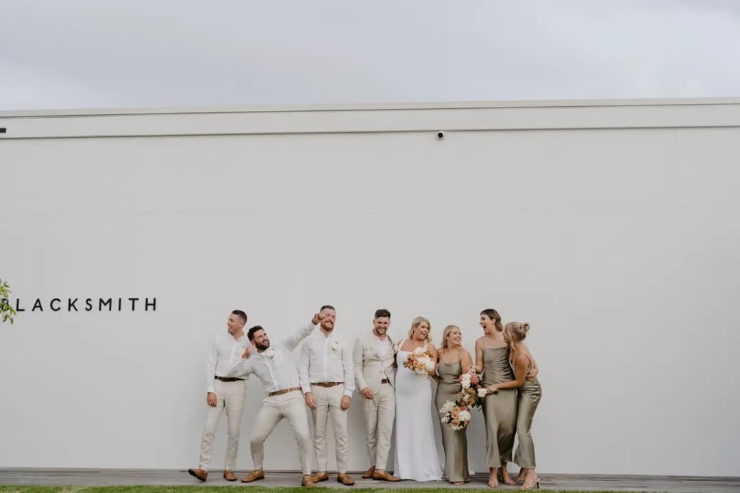 Wedding party laughing together against a white wall with Blacksmith lettering