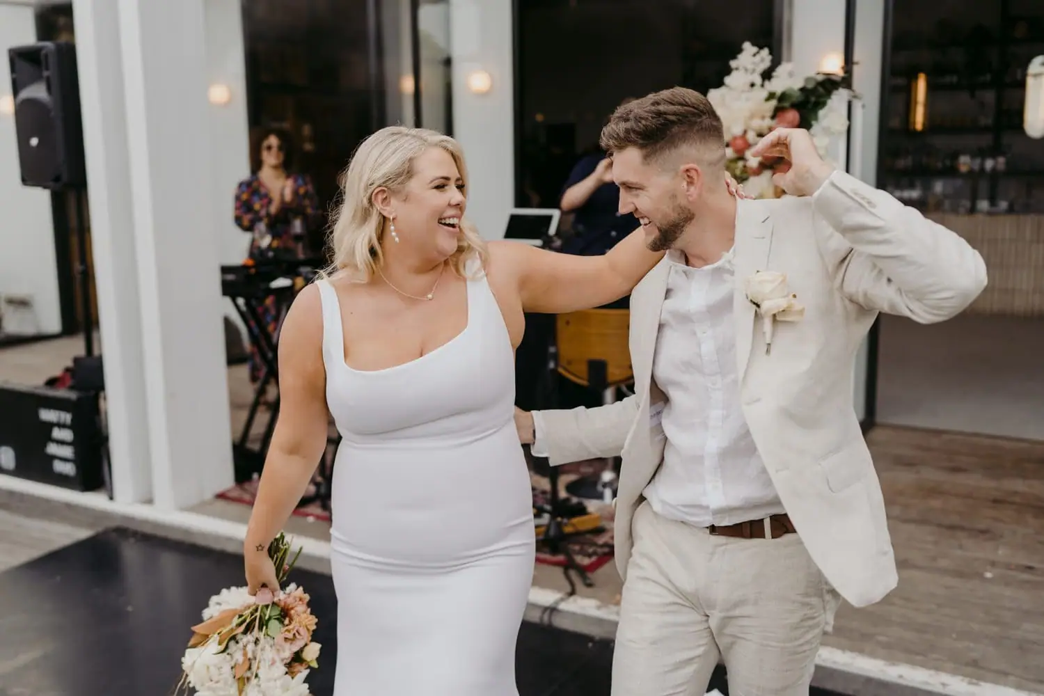 Bride laughing while resting her arm on the groom's shoulder outside the reception