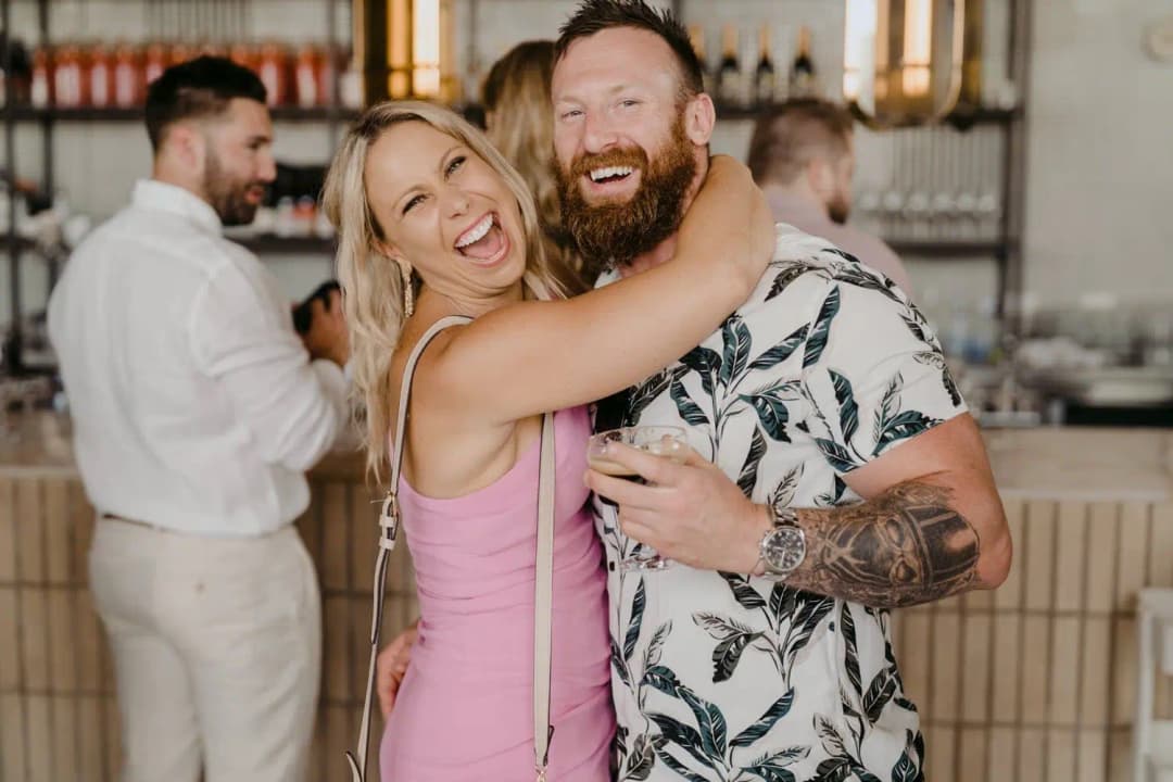 Two smiling wedding guests embracing beside the indoor bar
