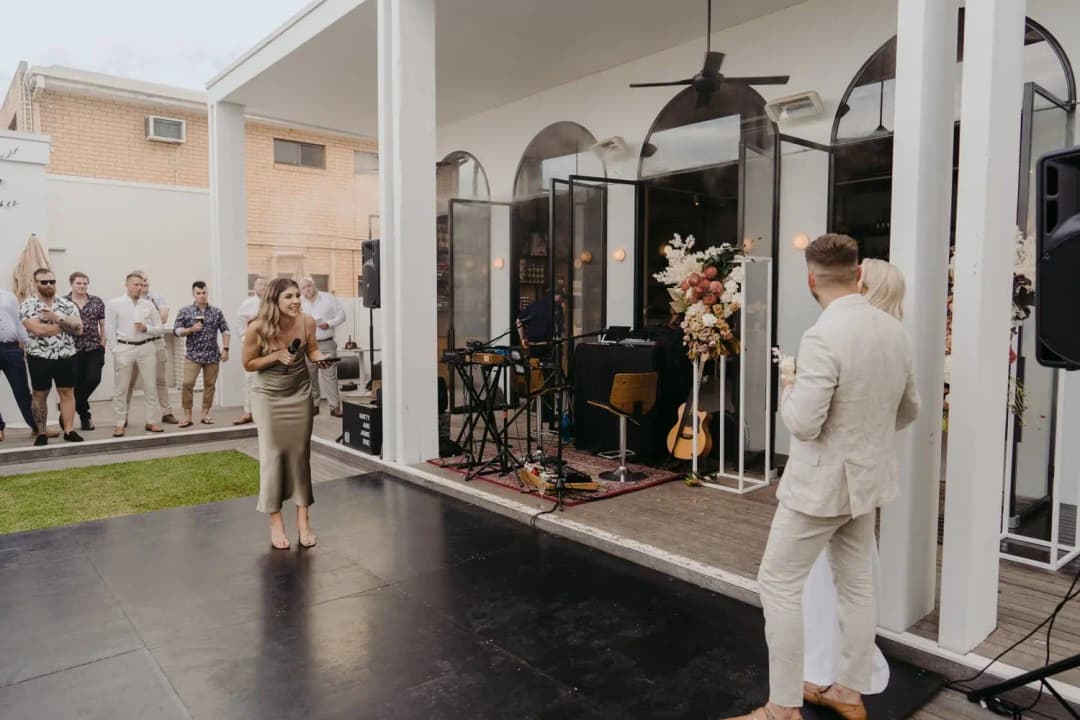 Bridesmaid speaking into a microphone as the couple listen outside the reception