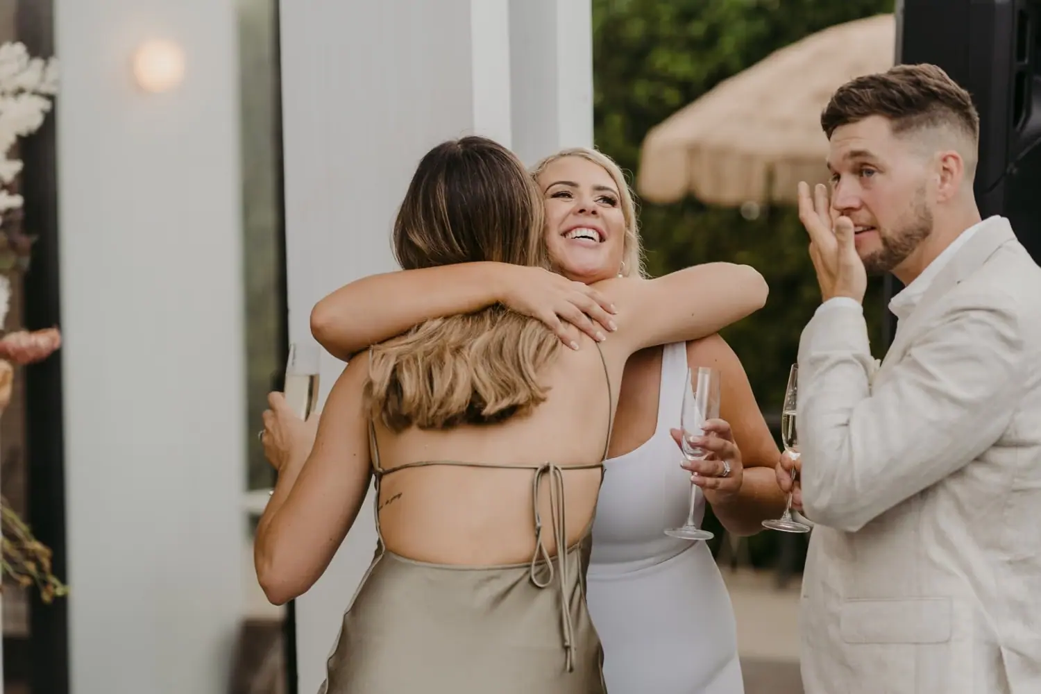 Bride hugging a bridesmaid as the groom wipes his eye beside them