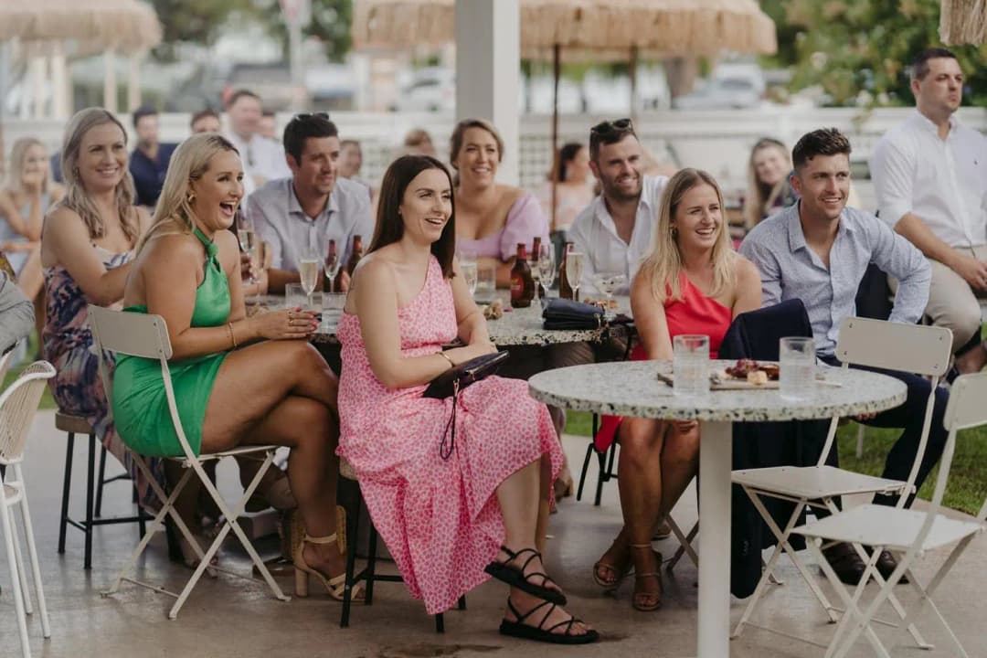 Seated wedding guests listening and smiling around outdoor tables