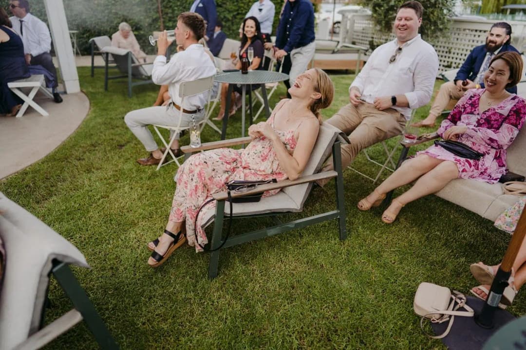 Guests laughing while seated on lawn chairs and a bench