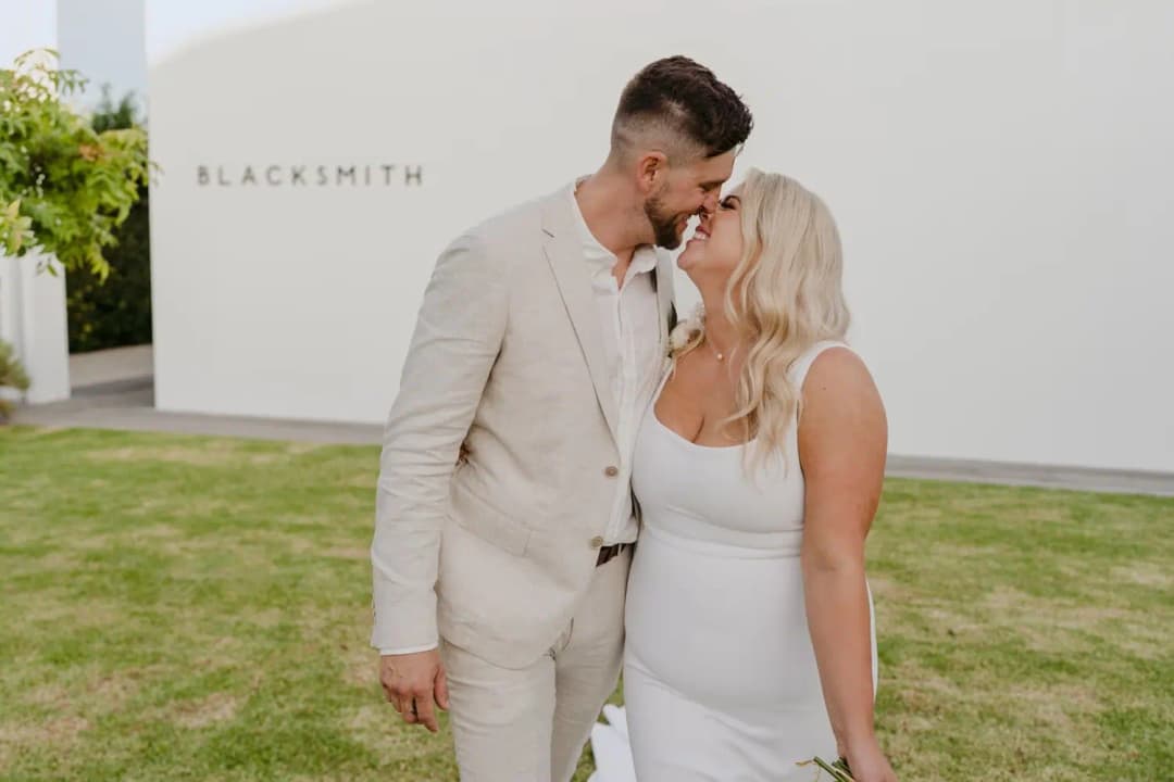 Bride and groom kissing on a lawn beside a white building