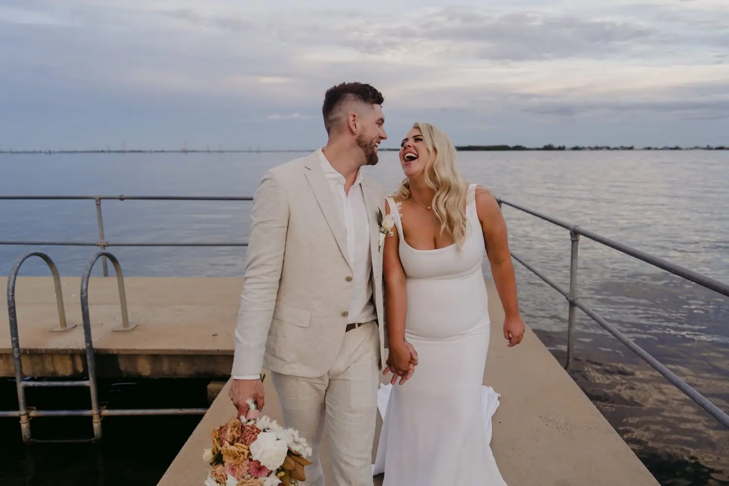 Bride and groom laughing together on a lakeside jetty