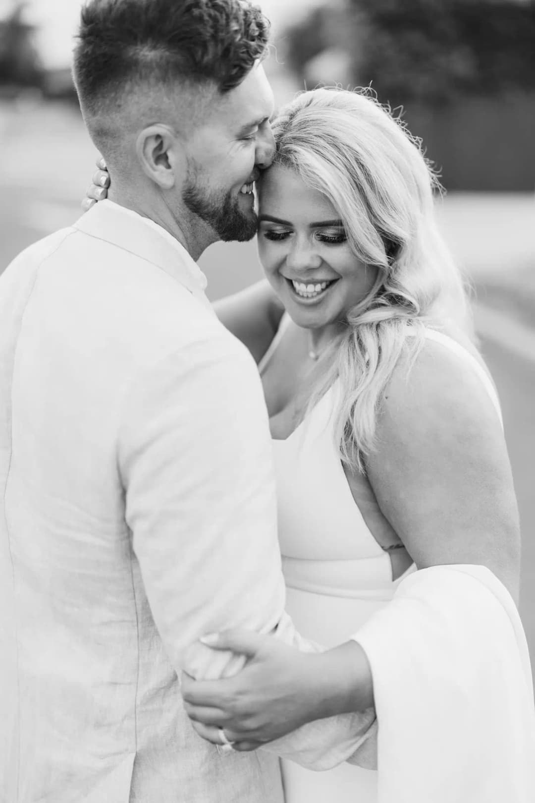 Black and white photograph of the groom kissing the smiling bride's forehead