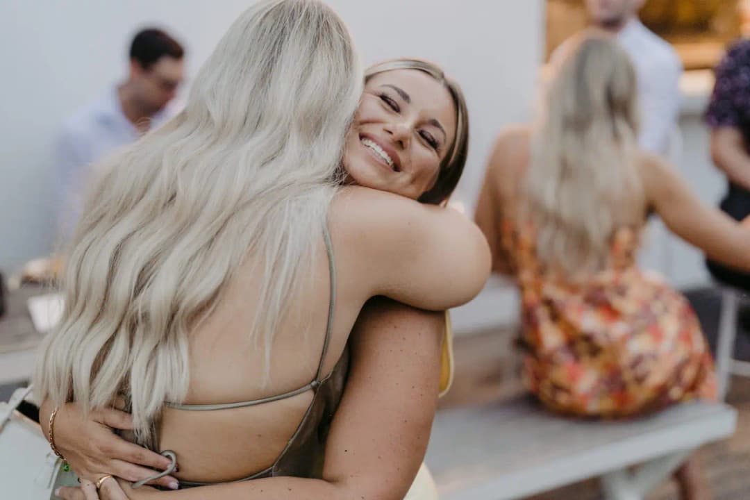 Two wedding guests hugging each other outdoors