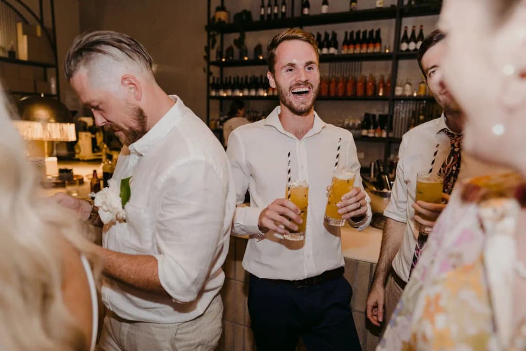 Men laughing and holding drinks beside the reception bar