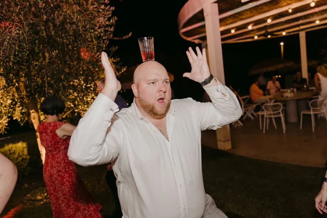 Guest balancing a glass on his head with both hands raised
