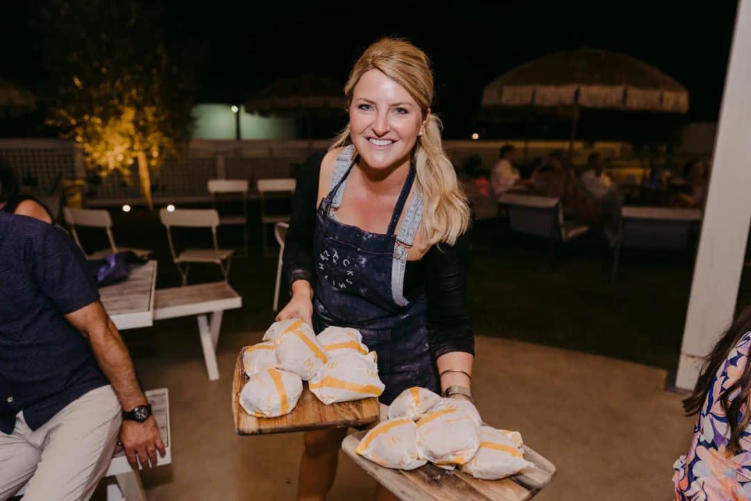 Smiling server carrying wooden boards of wrapped food outdoors