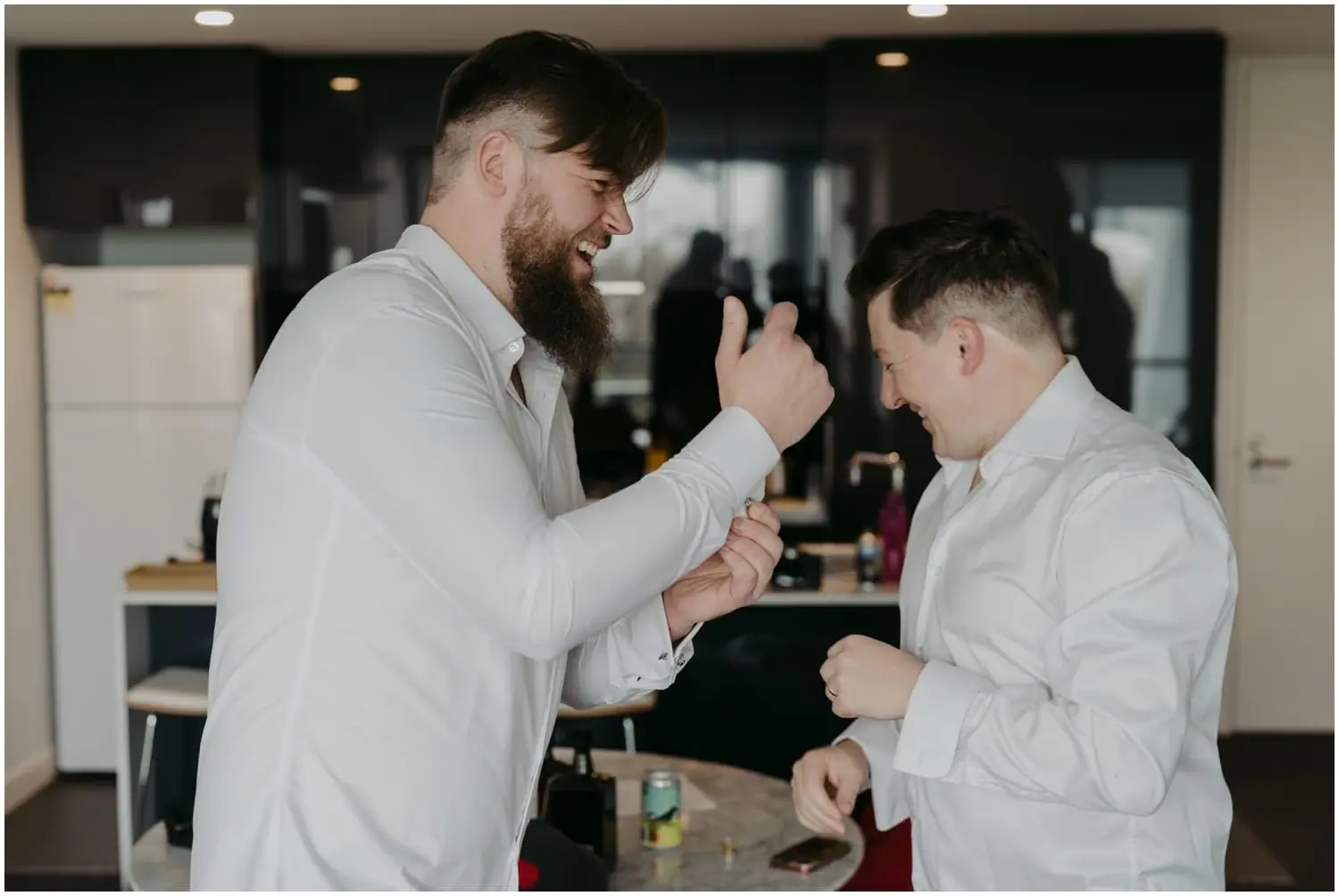 Two men laughing together in white shirts while getting ready