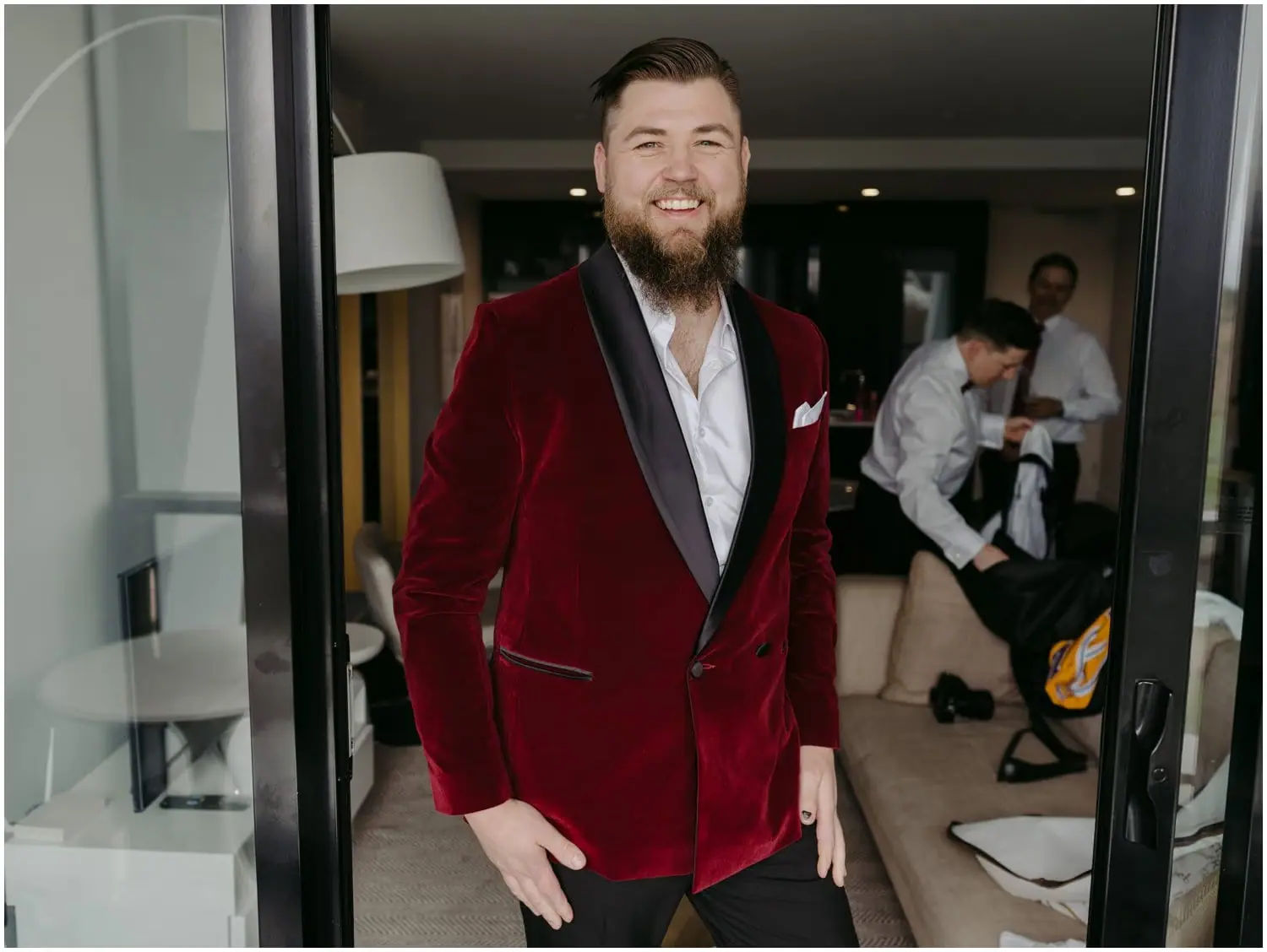 Groom smiling in a burgundy velvet jacket beside an open doorway