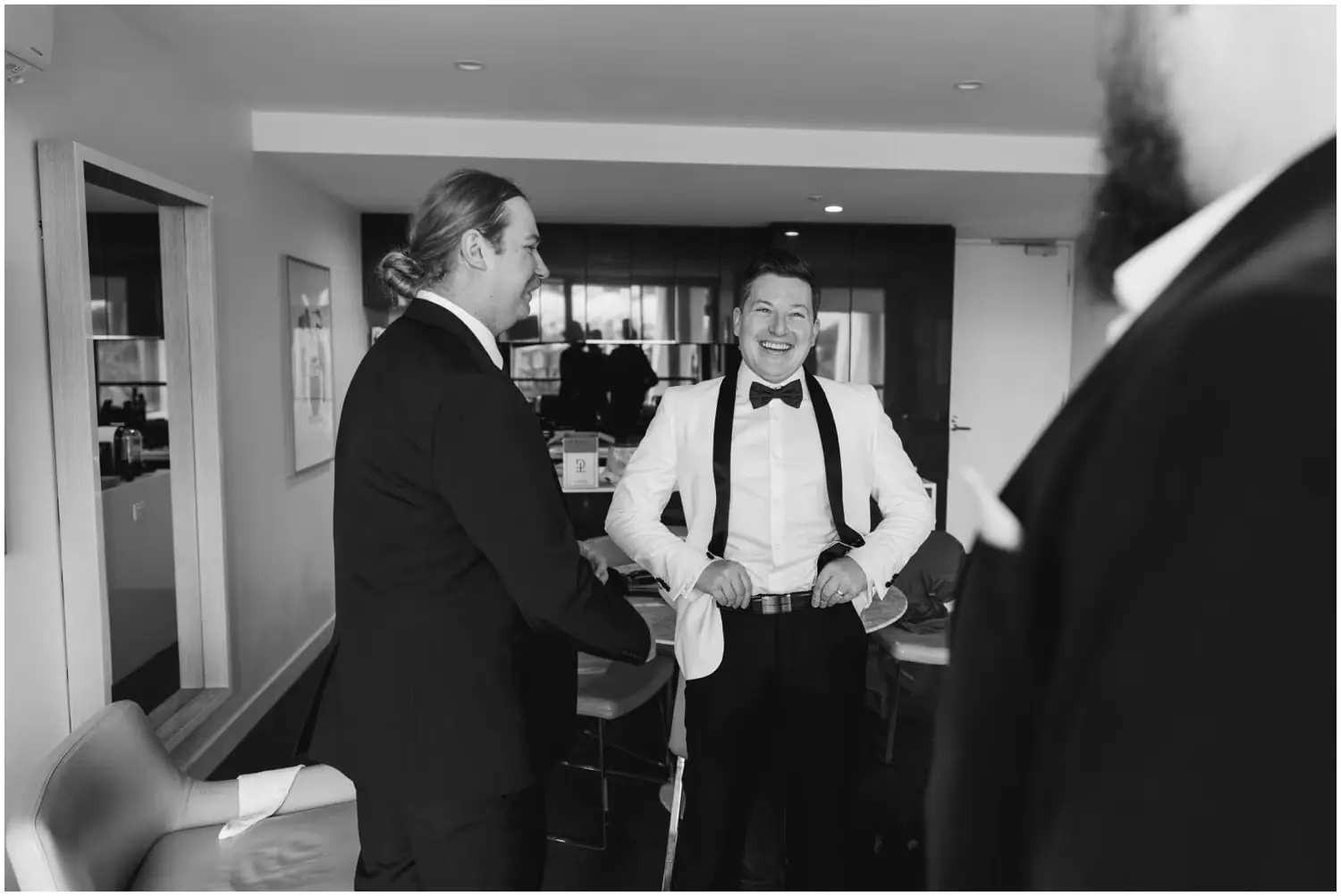 Black-and-white photograph of men chatting while dressing for the wedding