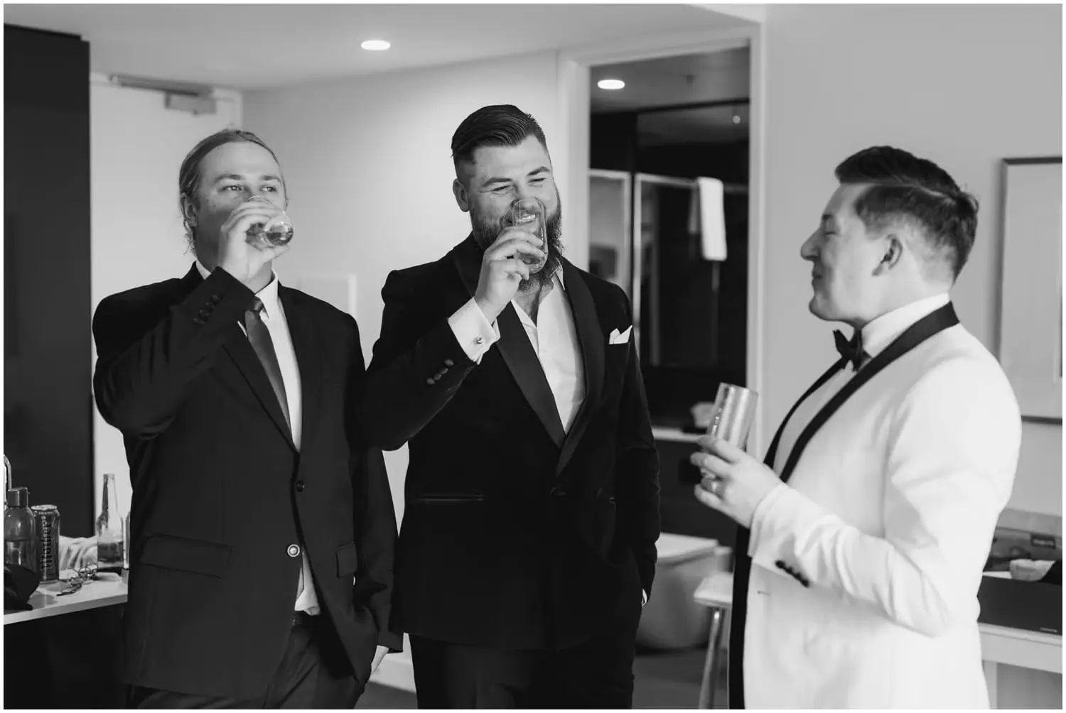 Black-and-white photograph of three men smiling and drinking together