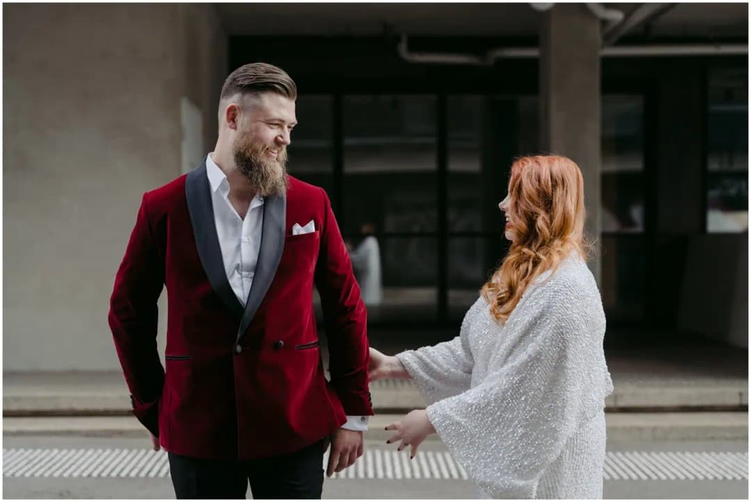 Groom turning toward the smiling bride outside a building