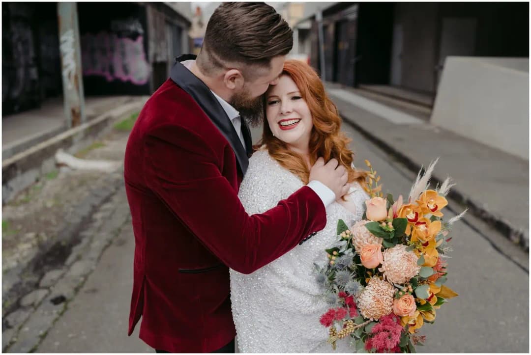Groom kissing the bride's forehead as she holds a colourful bouquet