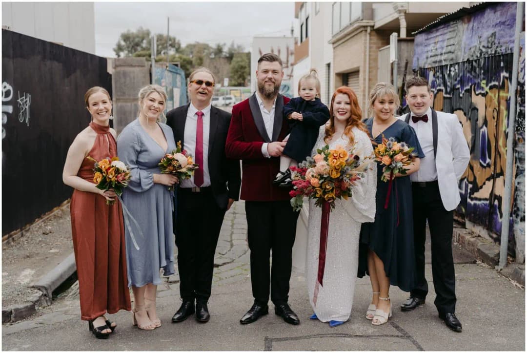 Wedding party standing together with a young child in a graffiti-lined laneway