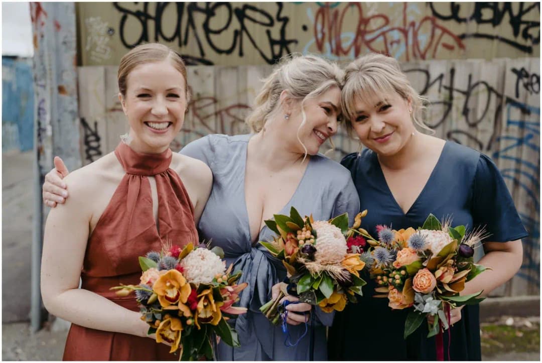 Three women leaning together and smiling with colourful bouquets
