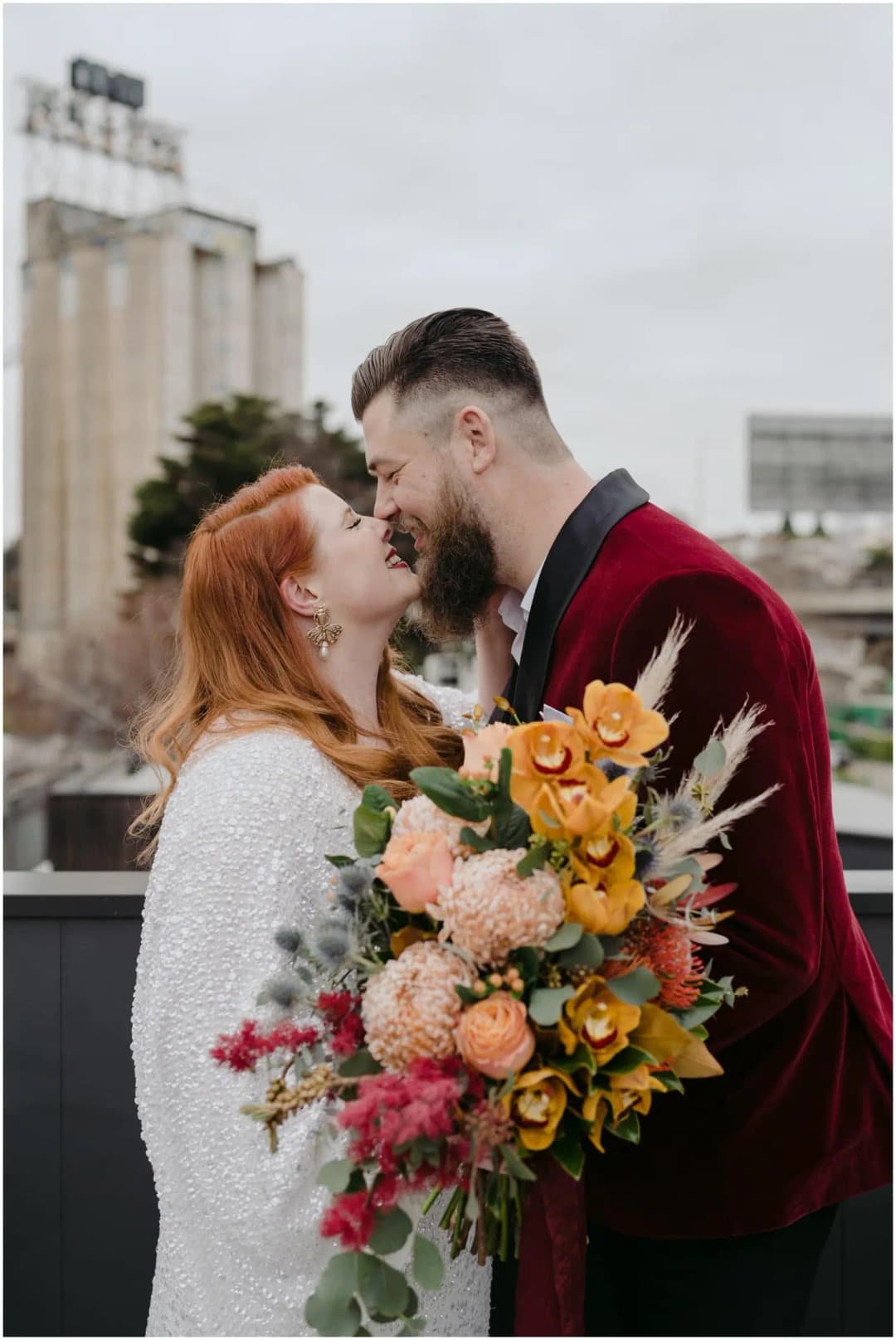 Bride and groom kissing while holding a colourful bouquet between them