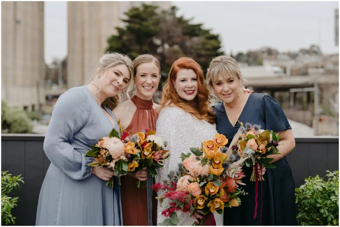 Bride and three friends leaning together with colourful bouquets