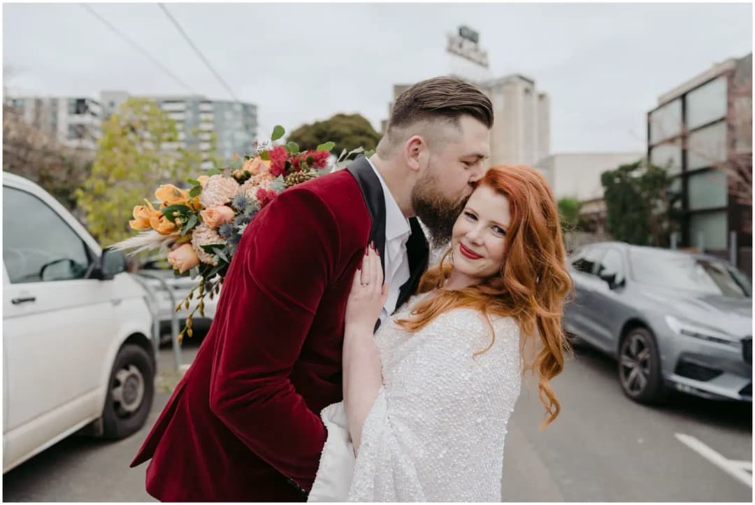 Groom kissing the smiling bride's forehead in a city street
