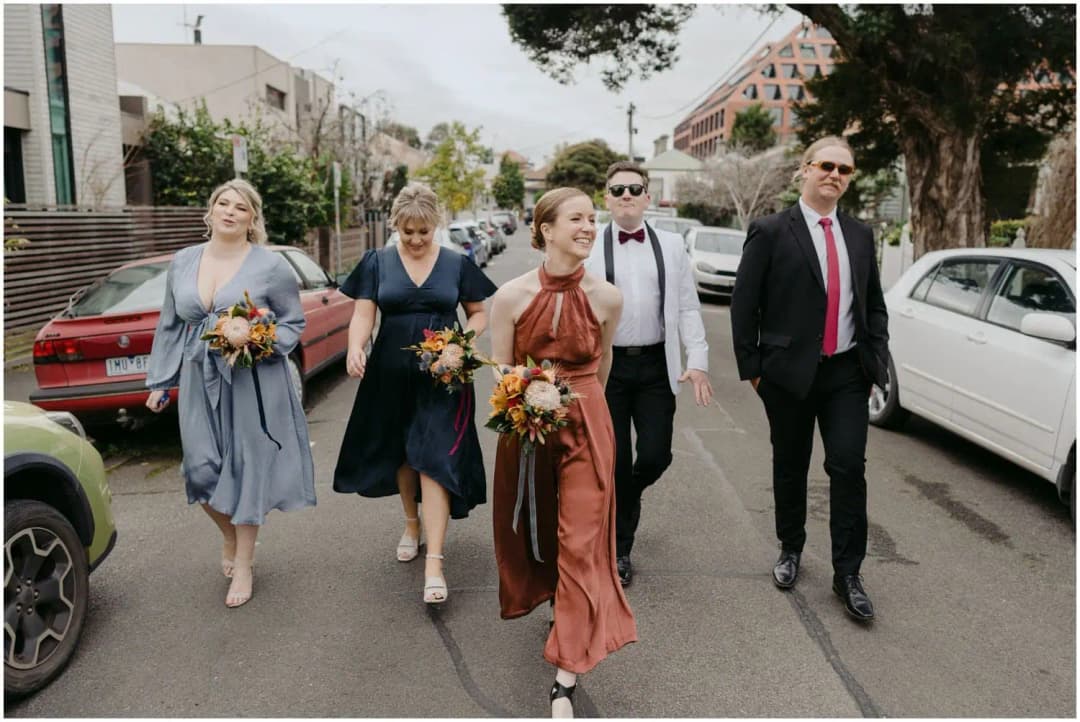 Wedding party walking along a street between parked cars