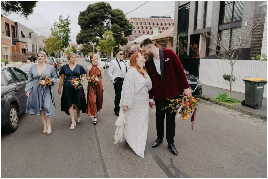 Bride and groom leaning toward a kiss while walking ahead of their friends