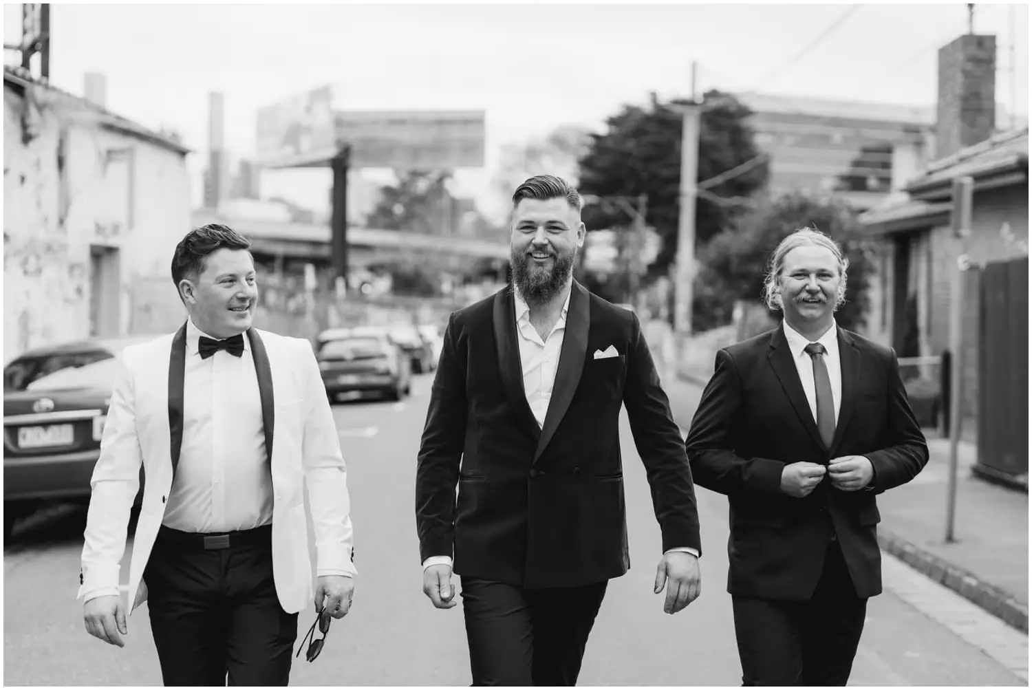 Black-and-white photograph of three men walking together along a city street