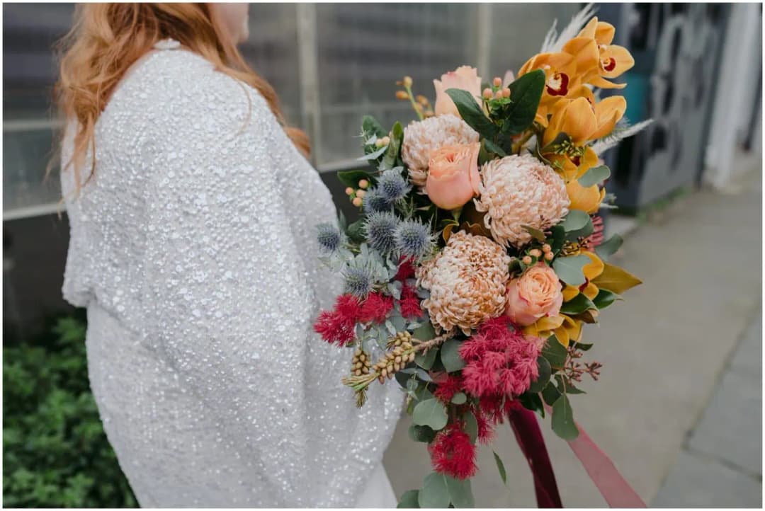 Close view of the bride's sparkling dress and colourful bouquet with trailing ribbons