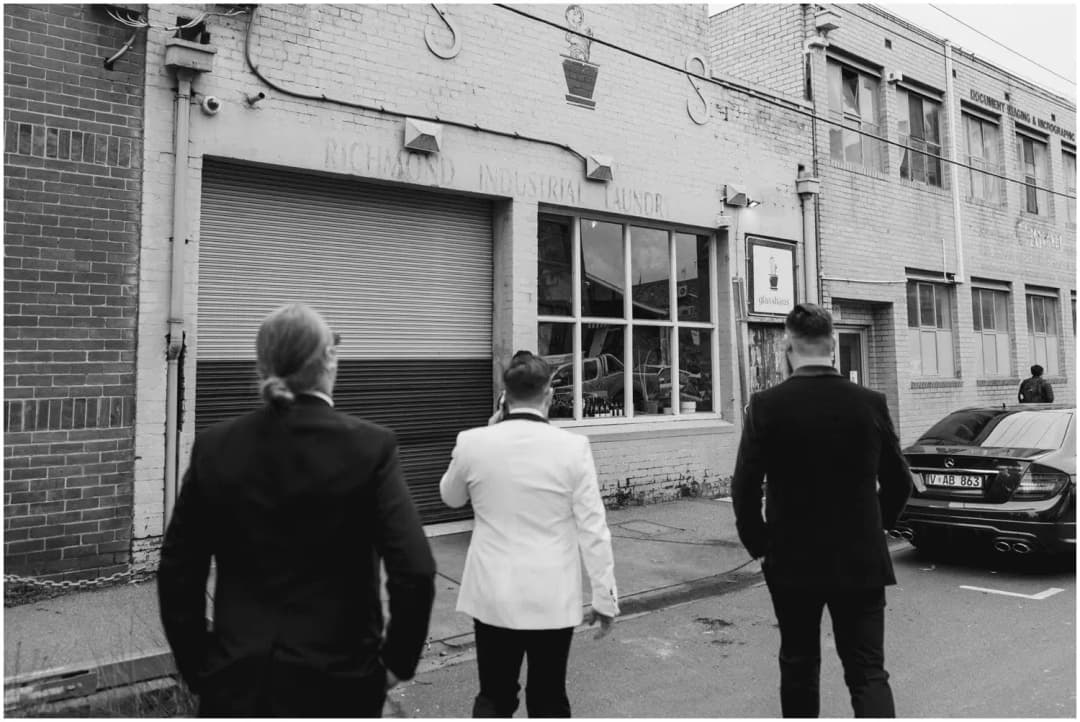 Black-and-white photograph of three men walking toward an industrial venue