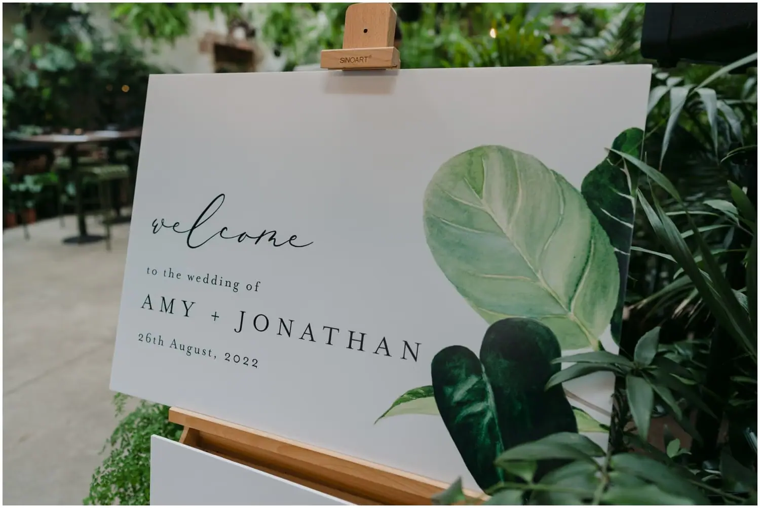 Wedding welcome sign on a wooden easel surrounded by green plants